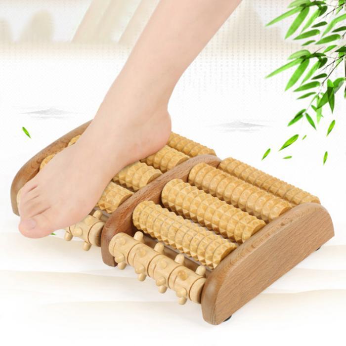 Wooden foot massager with a foot on it, surrounded by green leaves.